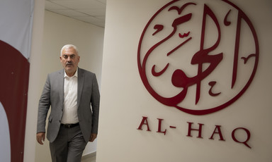 Man stands next to Al-Haq logo on wall