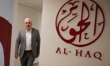 Man stands next to Al-Haq logo on wall