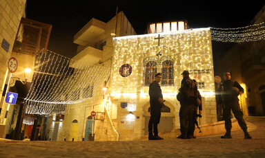 Soldiers carrying weapons stand beside an illuminated building 