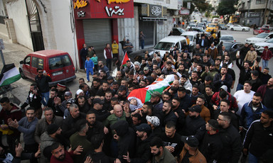 Body shrouded in Palestinian flag is carried on stretcher through city street by crowd of dozens