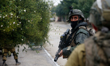 A soldier carrying a rifle looks at camera while standing on street