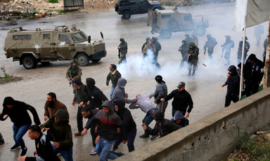 Men run away from Israeli soldiers shooting tear gas canisters in street