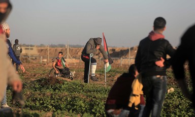 A protester in a wheelchair and another using crutches sit and stand near the Gaza-Israel boundary fence