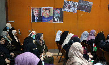 A group of people sit beneath three posters depicting British PM Boris Johnson, British minister Priti Patel and Arnold Balfour, who penned the Balfour declaration, giving away Palestine