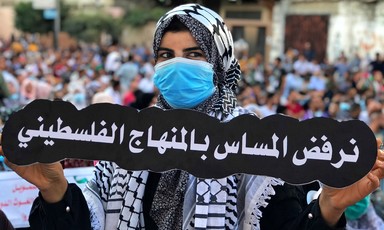 A woman in a face mask holds up a banner in Arabic