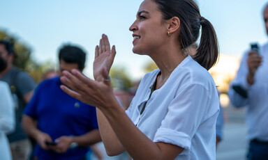 Woman speaks at microphone with onlookers behind her