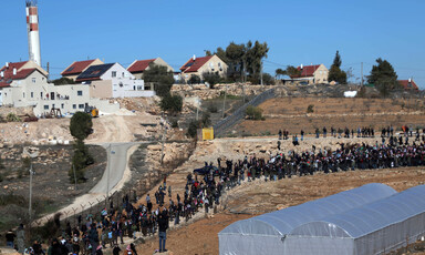 Landscape view shows hundreds of people walking along hillside with settlement homes in background