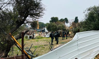 Armed forces stand in field near rubble and Hyundai bulldozer