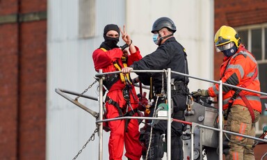 Man in handcuffs being removed by firefighters gives victory sign