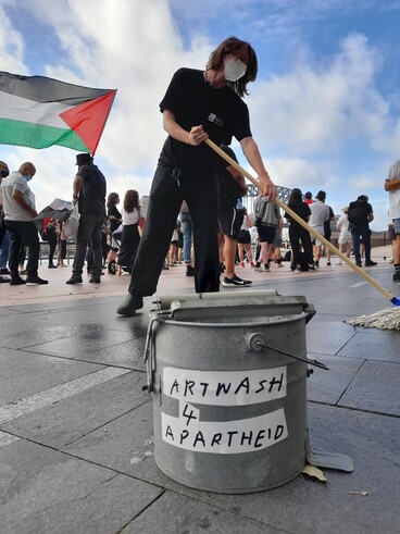 A protester mops the ground next to a bucket that says Artwash 4 Apartheid