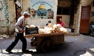 A man pushes a cart with bread in front of a poster depicting the al-Aqsa mosque in Jerusalem