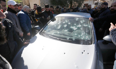 Men stand around silver car with windshield and hood pock-marked by bullet holes