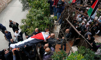 Mourners carry the body of a boy wrapped in a flag on a stretcher 