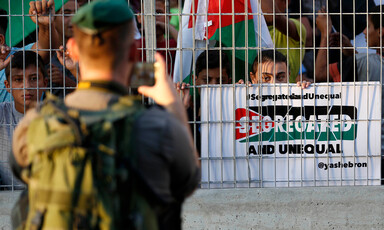 A soldier takes a picture of protestors separated by metal fence