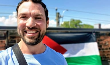A man smiles in front of a Palestinian flag