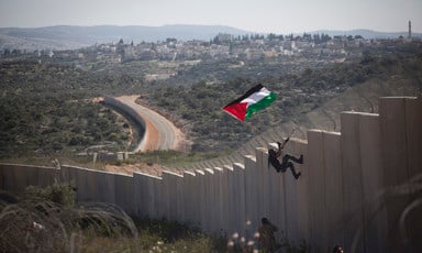 Landscape view of youth carrying Palestine flag scaling meters-high concrete wall