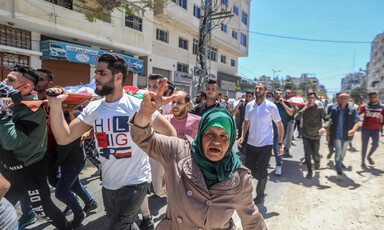 A older woman makes a victory sign with her hand while walking in funeral procession
