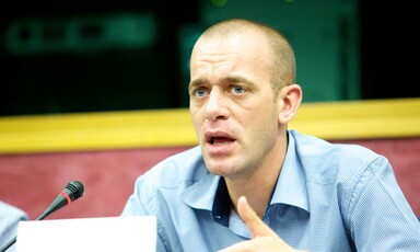 A man talks in front of a microphone and a name card 