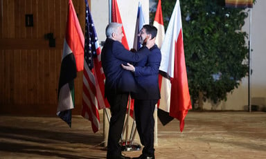 Two men in suits embrace in front of several flags 