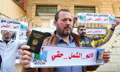 Man holds Arabic-language banner and Palestinian IDs during protest