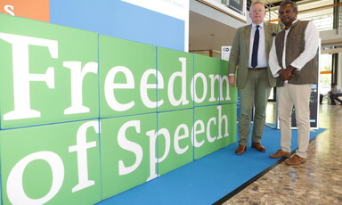 Two men stand next to banner reading freedom of speech