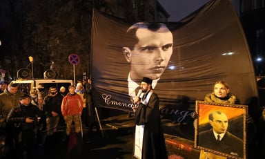 People watch a man in religious garb speak in front of a huge portrait of Stepan Bandera