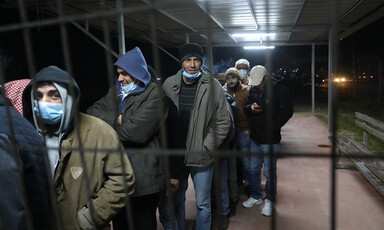Men, some wearing masks, line up behind a grille 