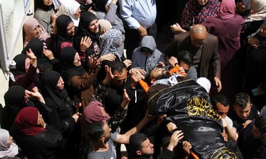 Crowd of men and women carry body of man wrapped in black flag on stretcher