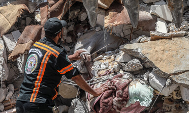 Civil defense worker touches arm protruding from under rubble