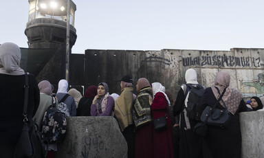 Women stand in front of concrete wall and military watchtower