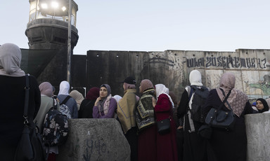 Women stand in front of concrete wall and military watchtower