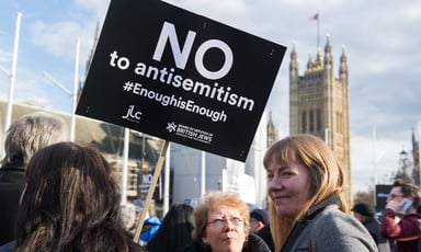 Two women can be seen beside a placard bearing the words No to antisemism enough is enough