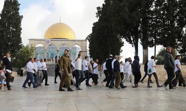Men wearing religious accoutrements walk in front of the Dome of the Rock