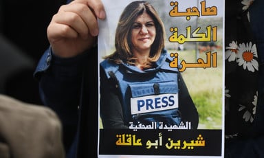 Close-up of a hand holding a poster of Shireen Abu Akleh wearing a press vest