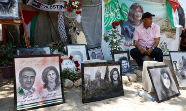 A man sits surrounded by drawings and posters of Shireen Abu Akleh