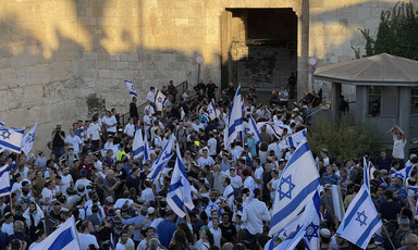 Large group of people with flags against backdrop of ancient stone wall