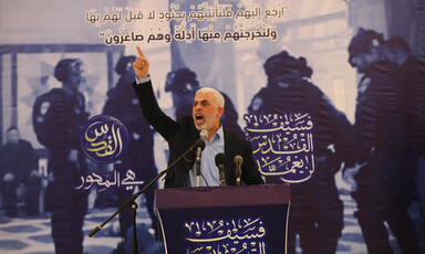 Man in a suit gives a speech at a podium against a backdrop 