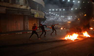 Three masked men wield slingshots next to a fire