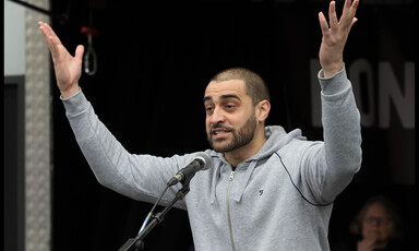 A man raises his arms while speaking into a microphone