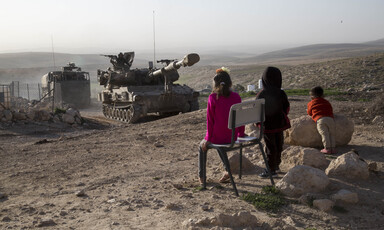 Children stand in front of tank on rocky hilltop