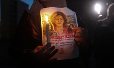 Close-up of pair of hands holding a candle and poster of Shireen Abu Akleh