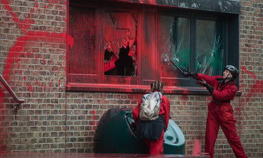 A woman smashes windows of an office building daubed with red paint
