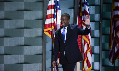 Man waves with American flags behind him
