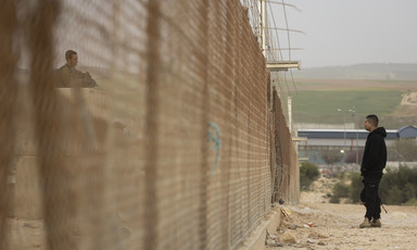 Man faces soldier standing in guard tower behind tall fence topped with barbed wire
