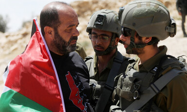 A man with a Palestinian flag confronts two soldiers