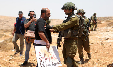 A man holding a sign is pushed by an Israeli soldier