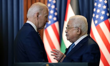 Mahmoud Abbas gestures with his hand while speaking with Joe Biden as they stand in front of US and Palestinian flags