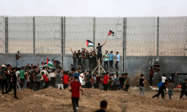 Crowd stands near militarized fence holding Palestine flags