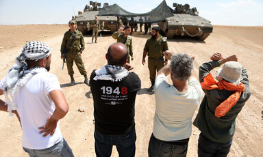 A group of young men confronts soldiers standing beside tanks