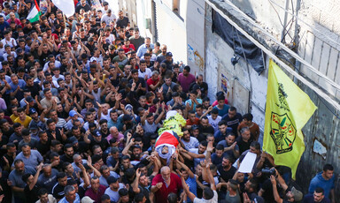 Dozens of people carry the body of a boy. wrapped in a flag on a stretcher 